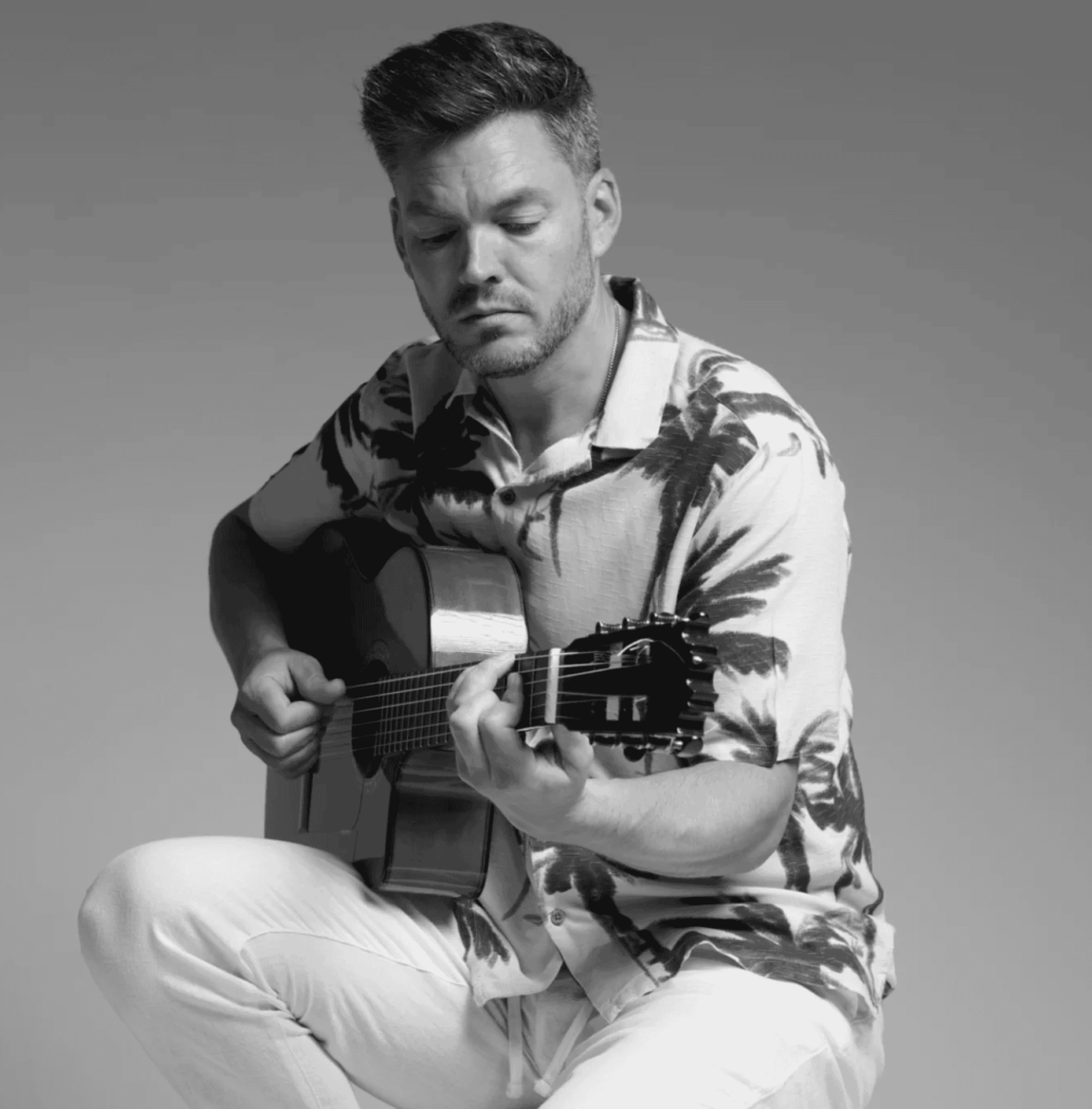Retrato en blanco y negro de un músico sentado tocando la guitarra.