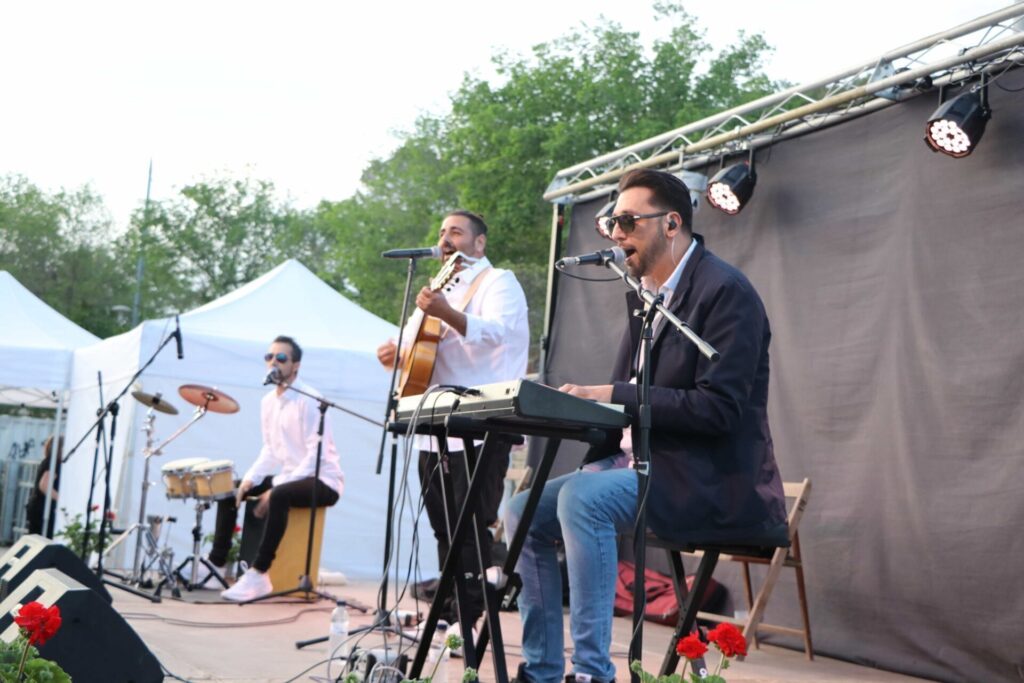 Drei Musiker mit Keyboard, Gitarre und Percussion auf einer Außenbühne.