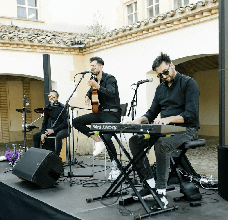 Músicos con guitarra, teclado y percusión durante una actuación en un patio.