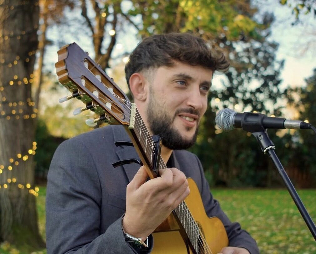 Guitarrista cantando ante un micrófono en un jardín.