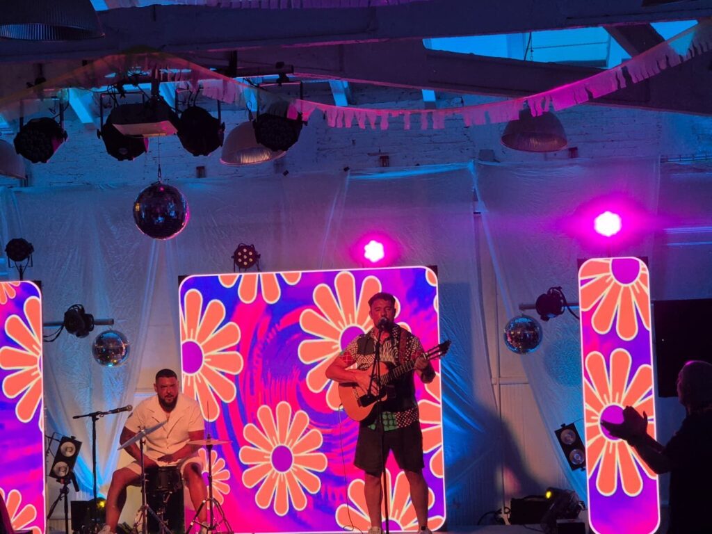 Gitarrist und Percussionist auf einer Bühne mit bunten Lichtern.