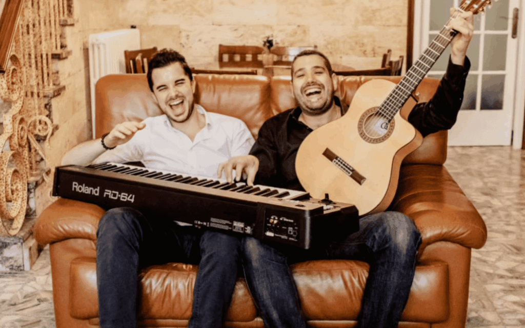 Dos músicos con guitarra y teclado sentados en un sofá.