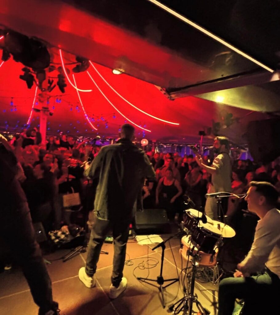 Músicos en un escenario frente al público, con iluminación roja.