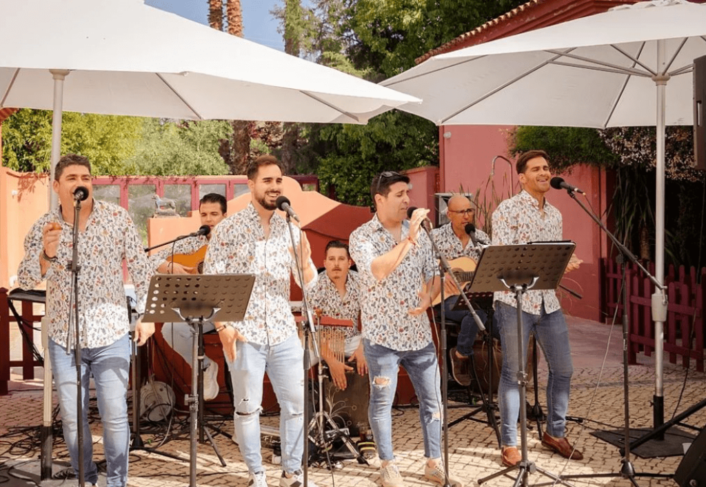 Formación musical con varias voces, guitarras y percusión al aire libre.