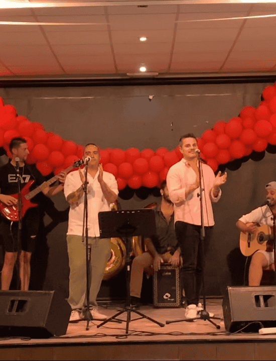 Cantantes y músicos en un escenario con decoración de globos rojos.